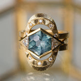 Gold ring with a central blue Montana sapphire and diamond accents on a reflective surface.
